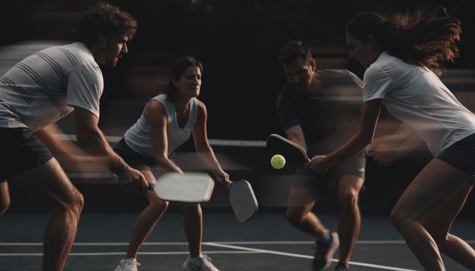 Four players in a doubles rally, two at the kitchen line trading dinks. Representative lifestyle image.